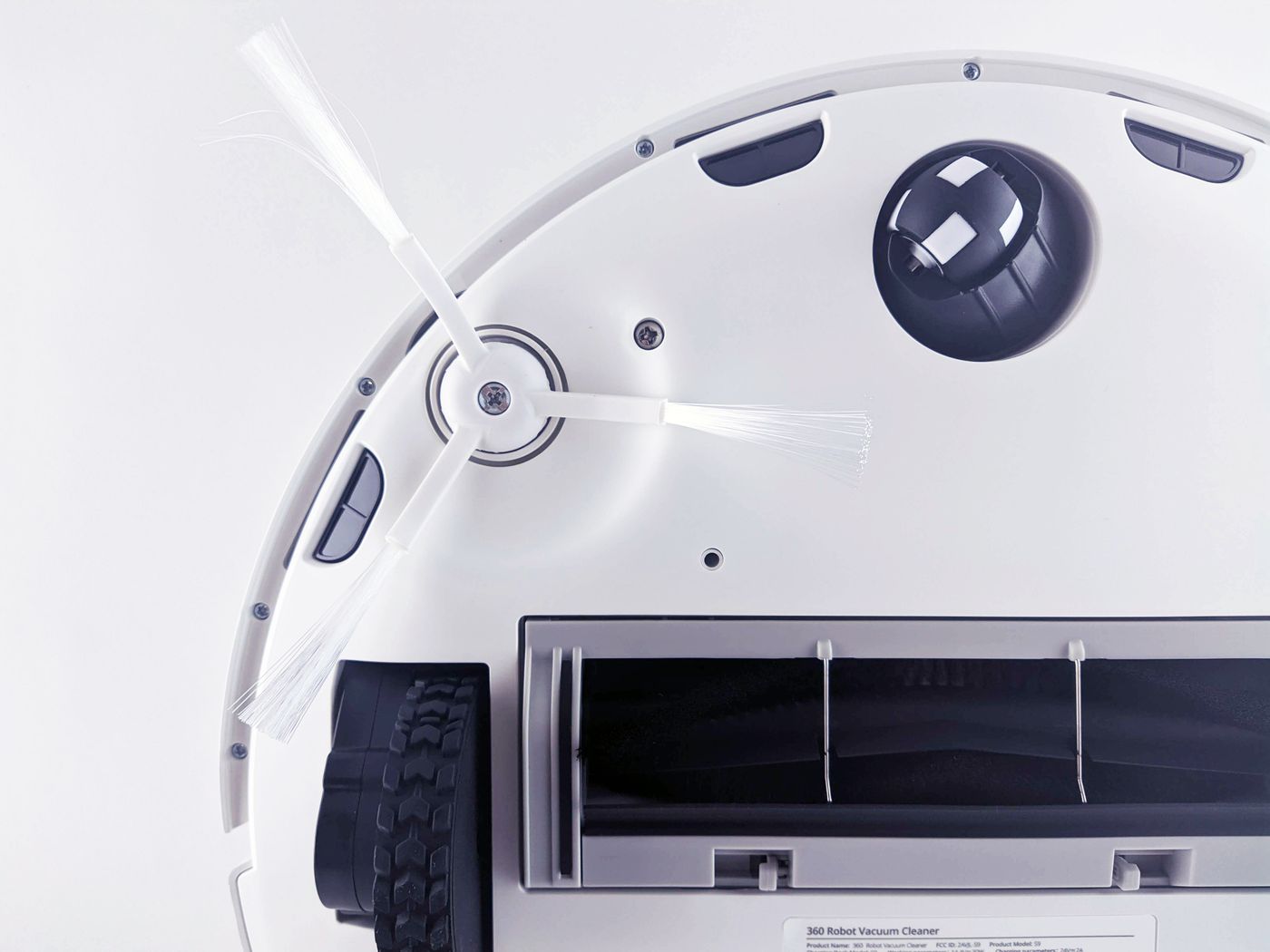 Underside of a white robot vacuum showing a wheel and side brush.