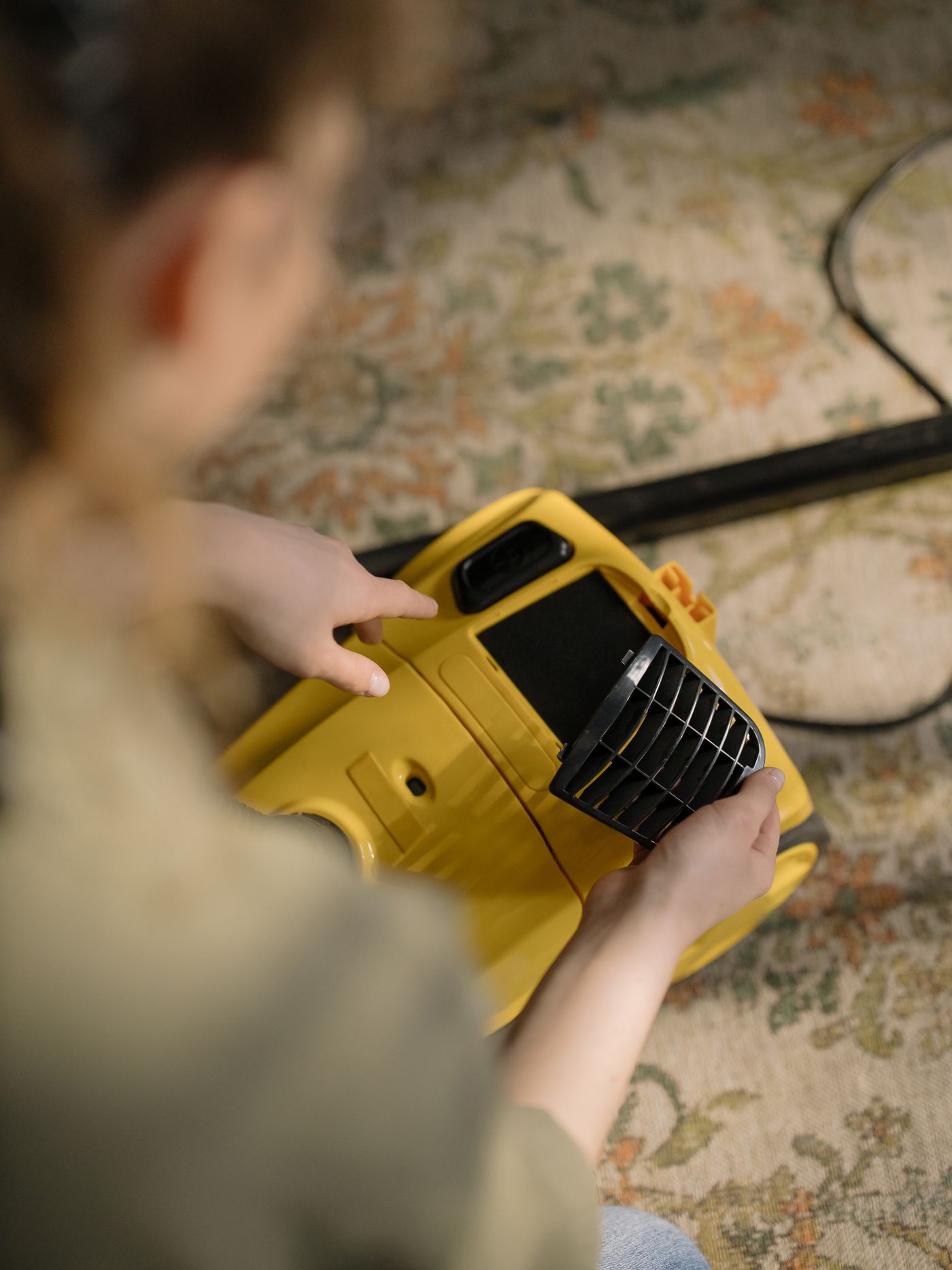 Person handling a filter cover on a yellow vacuum cleaner.