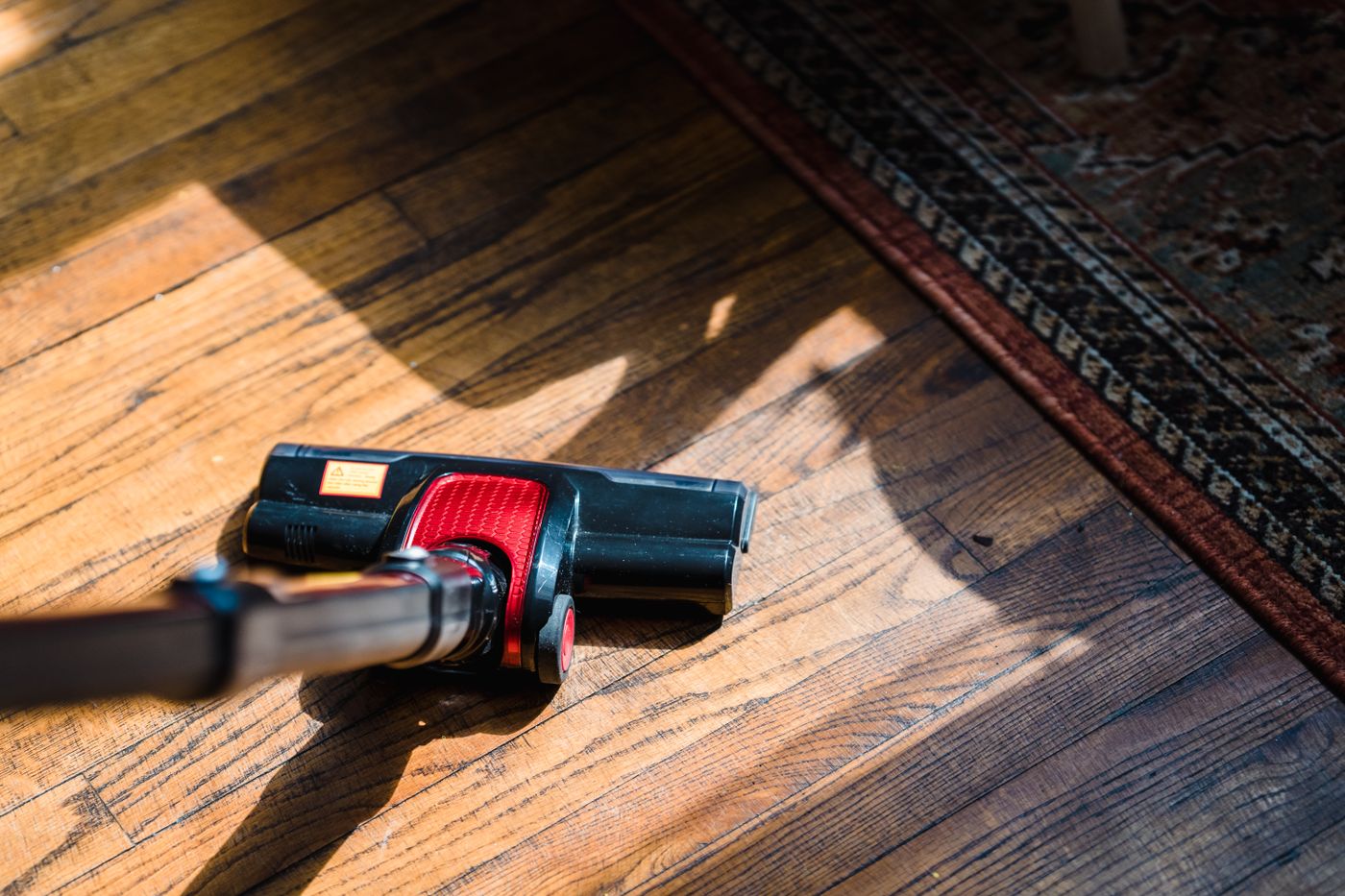 Red and black vacuum floorhead on a wooden floor beside a rug.
